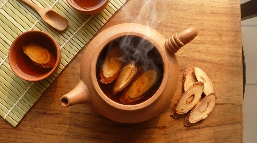 Red Tongkat Ali root slices being brewed in a traditional ceramic pot, producing deep amber tea
